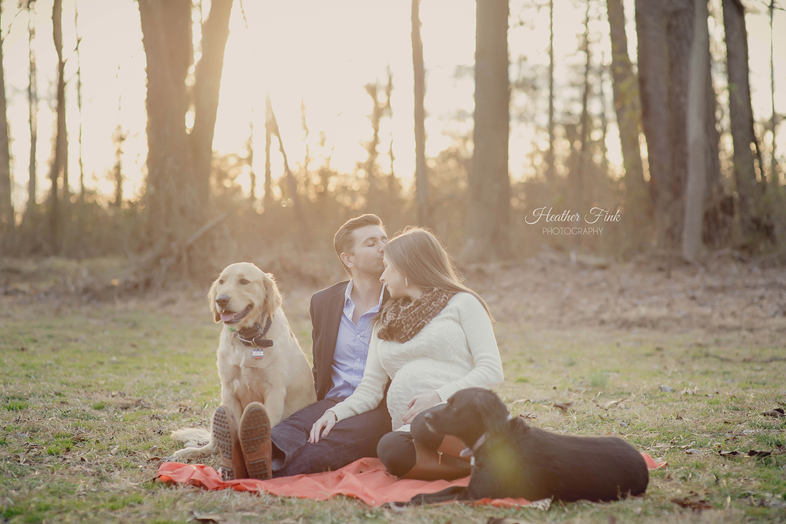 pregnant couple kissing while sitting with dogs