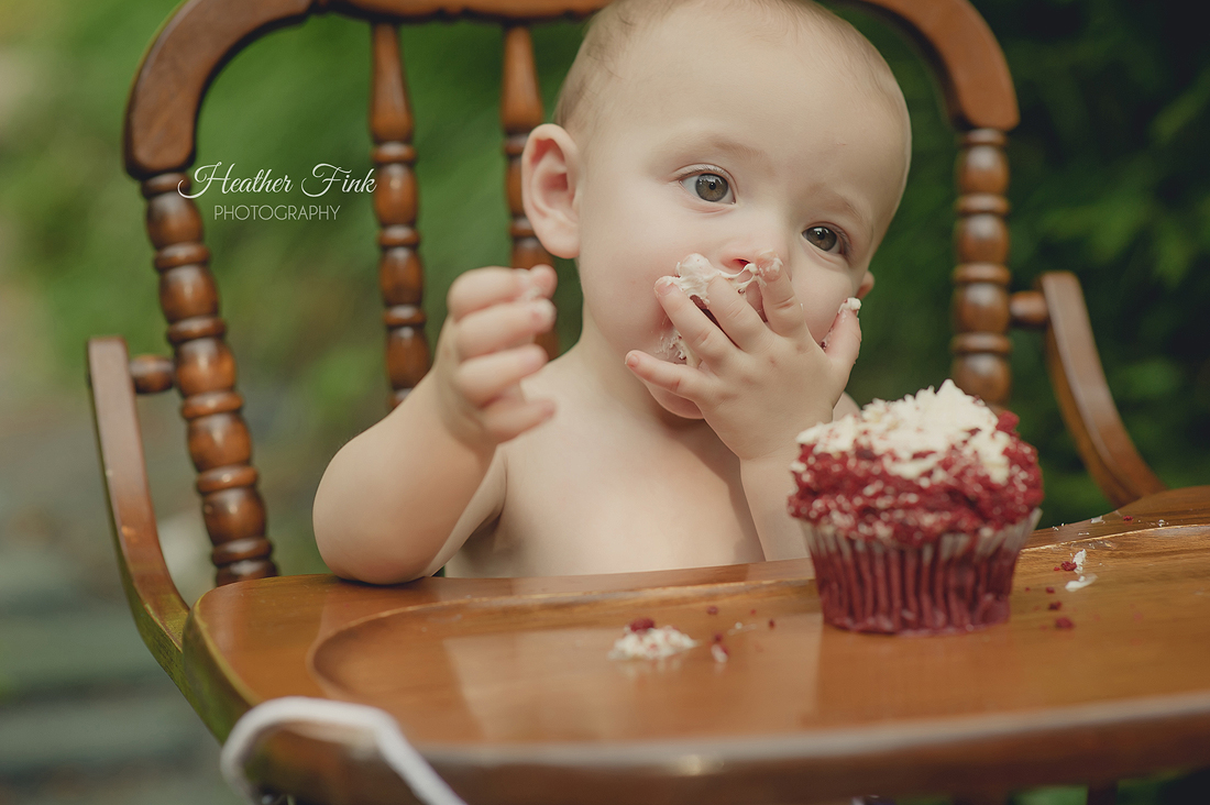 one year old boy enjoys eating cupcake in high chair